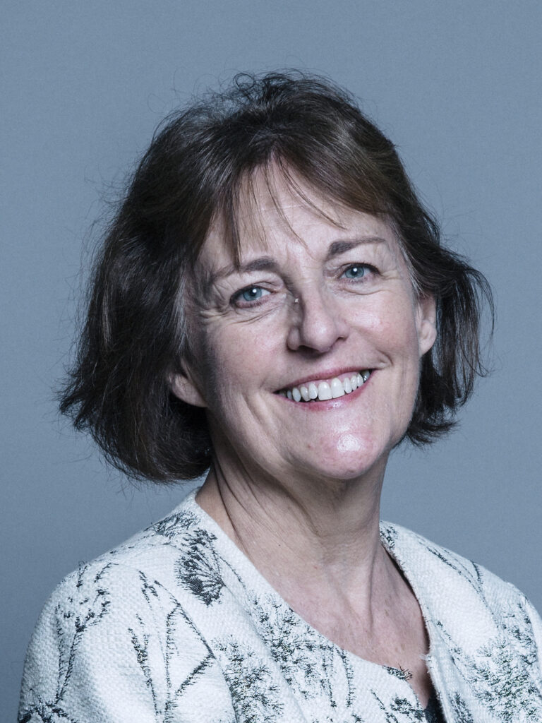 Portrait of a woman with short, dark hair, wearing a light-coloured, textured sweater against a plain grey background.