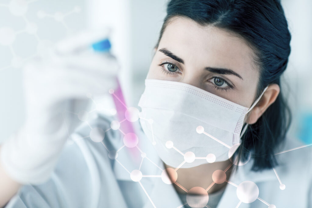 A young researcher wearing gloves and a lab coat, examines a test tube.