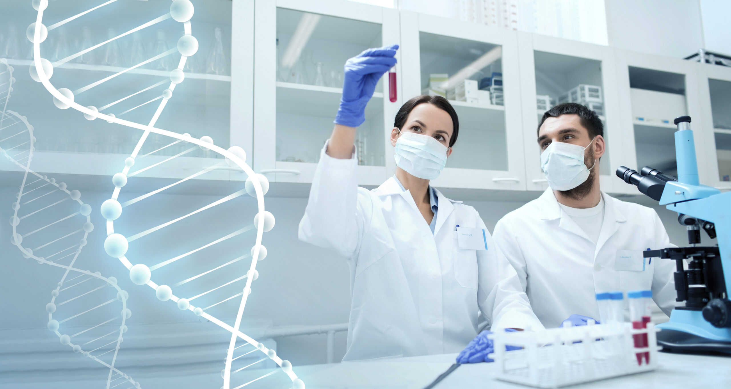 Two researchers analysing a test tube with a red liquid, in a lab. A representation of DNA is shown on the left. 
