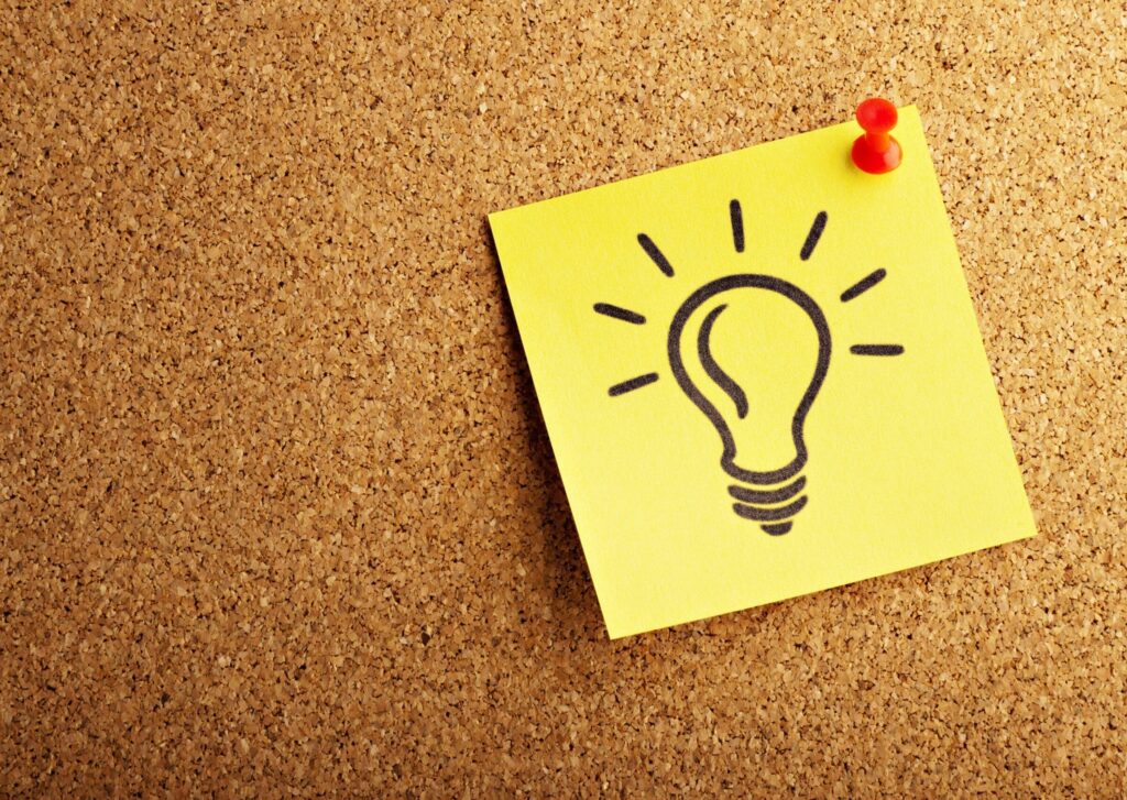 A post-it note with a graphic of a light bulb, pinned to a cork board.