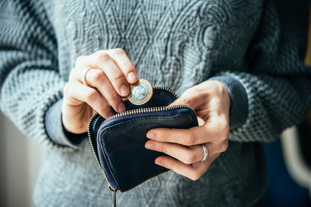 A person putting a pound coin away in a black zip-up wallet.