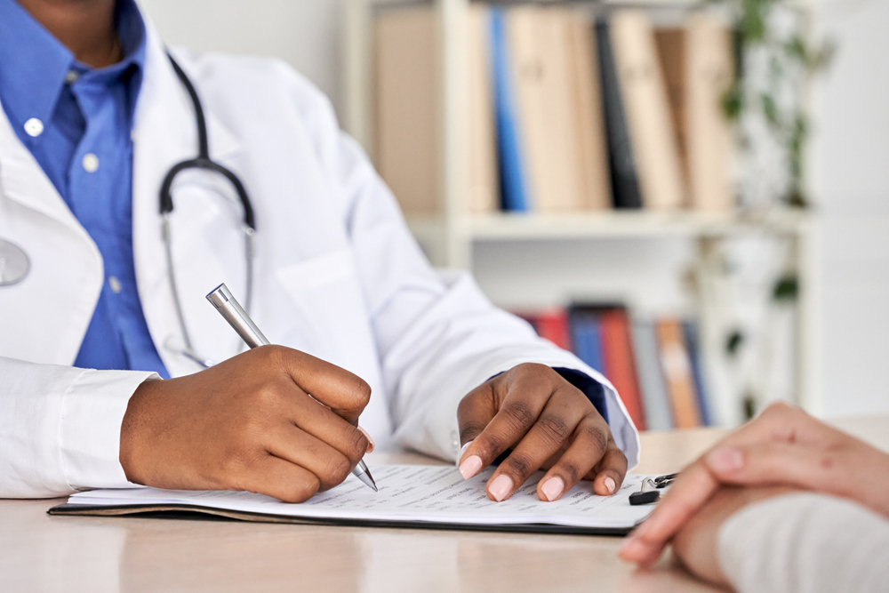 A doctor writes notes on a clipboard, whilst speaking with a patient.