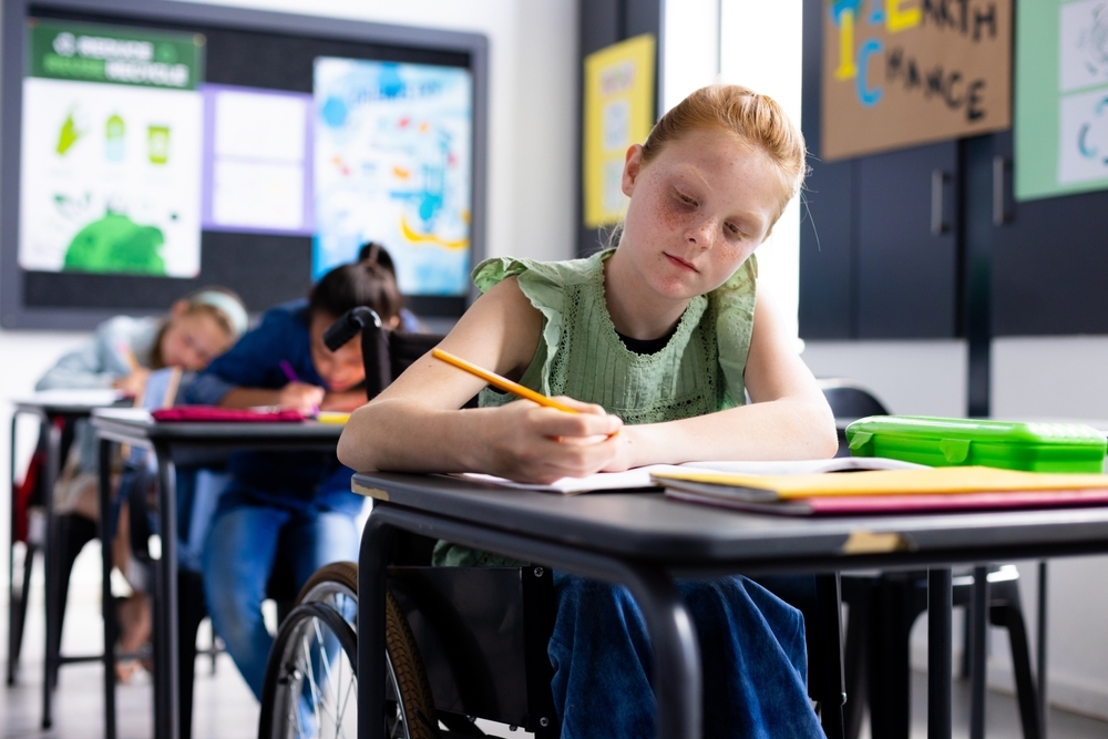 A young, disabled person in a wheelchair, working in school.