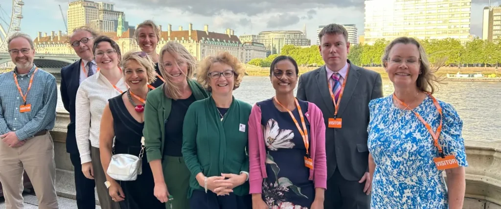 Members and attendees of the APPG's on ME and Long Covid smiling, standing in front of the River Thames in London.
