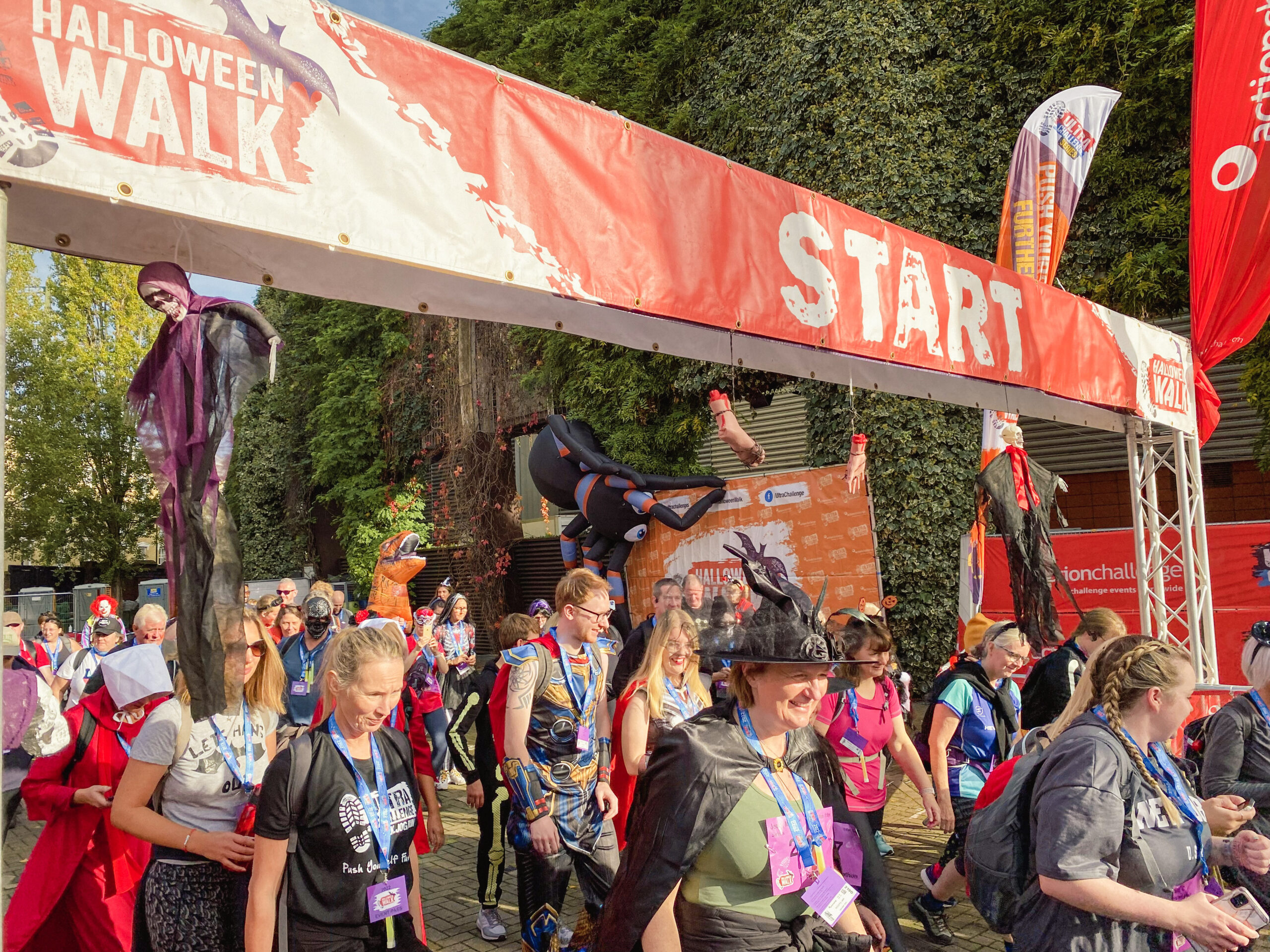 Participants in Halloween costumes walking under a red 'START' banner at an outdoor event.