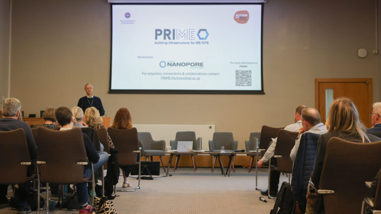 A speaker addresses attendees beneath a PRIME presentation screen at the 2026 symposium in Edinburgh.